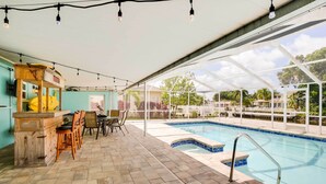 An indoor pool area with a tiled floor, a pool with a blue tile border, a wooden bar area, and a covered seating area with chairs. - Canal-front Tampa Vacation Rental w/ Private Pool! (Tampa)