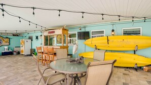 A dining area with a round table and chairs, a wooden bar counter, and two yellow surfboards against the wall. - Canal-front Tampa Vacation Rental w/ Private Pool! (Tampa)