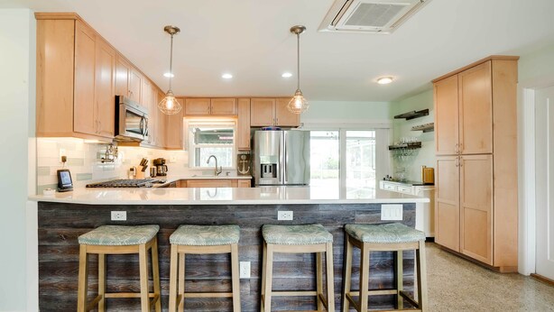 A modern kitchen with wooden cabinets, a central island with stools, stainless steel appliances, and pendant lighting. - Canal-front Tampa Vacation Rental w/ Private Pool! (Tampa)