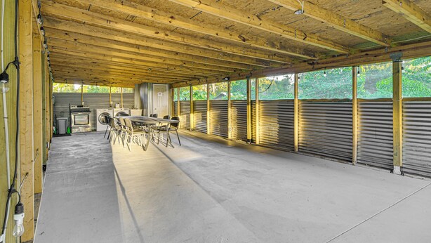 Un espace extérieur abrité doté d’un sol en béton, de poutres en bois au plafond et de volets métalliques le long d’un des murs.