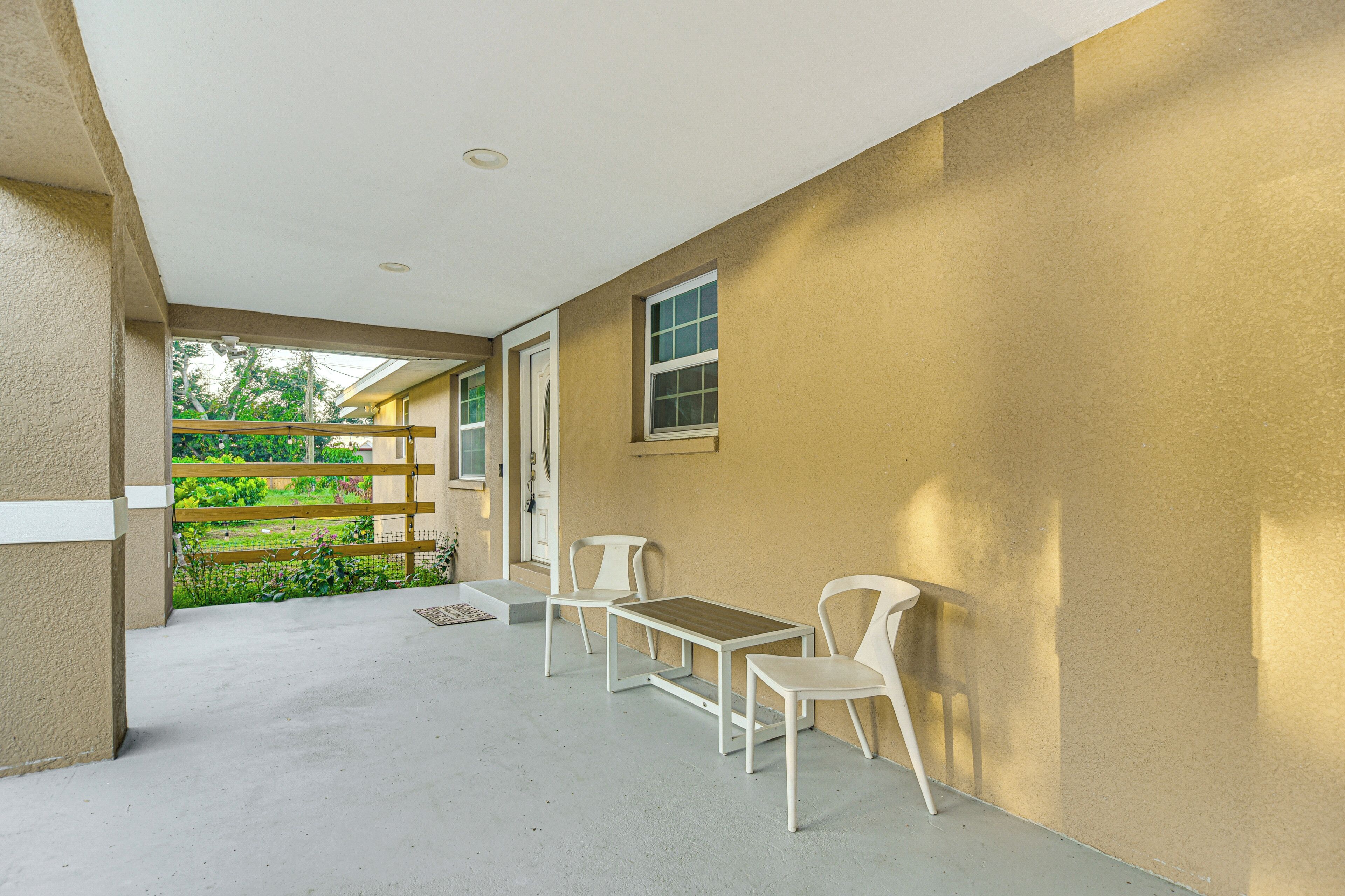 A covered outdoor area with a concrete floor, a wooden bench, a table, and two chairs.