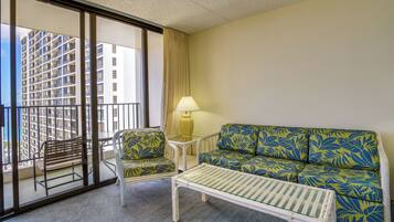 A hotel room with a balcony, a sofa, a chair, a small table, and a lamp.