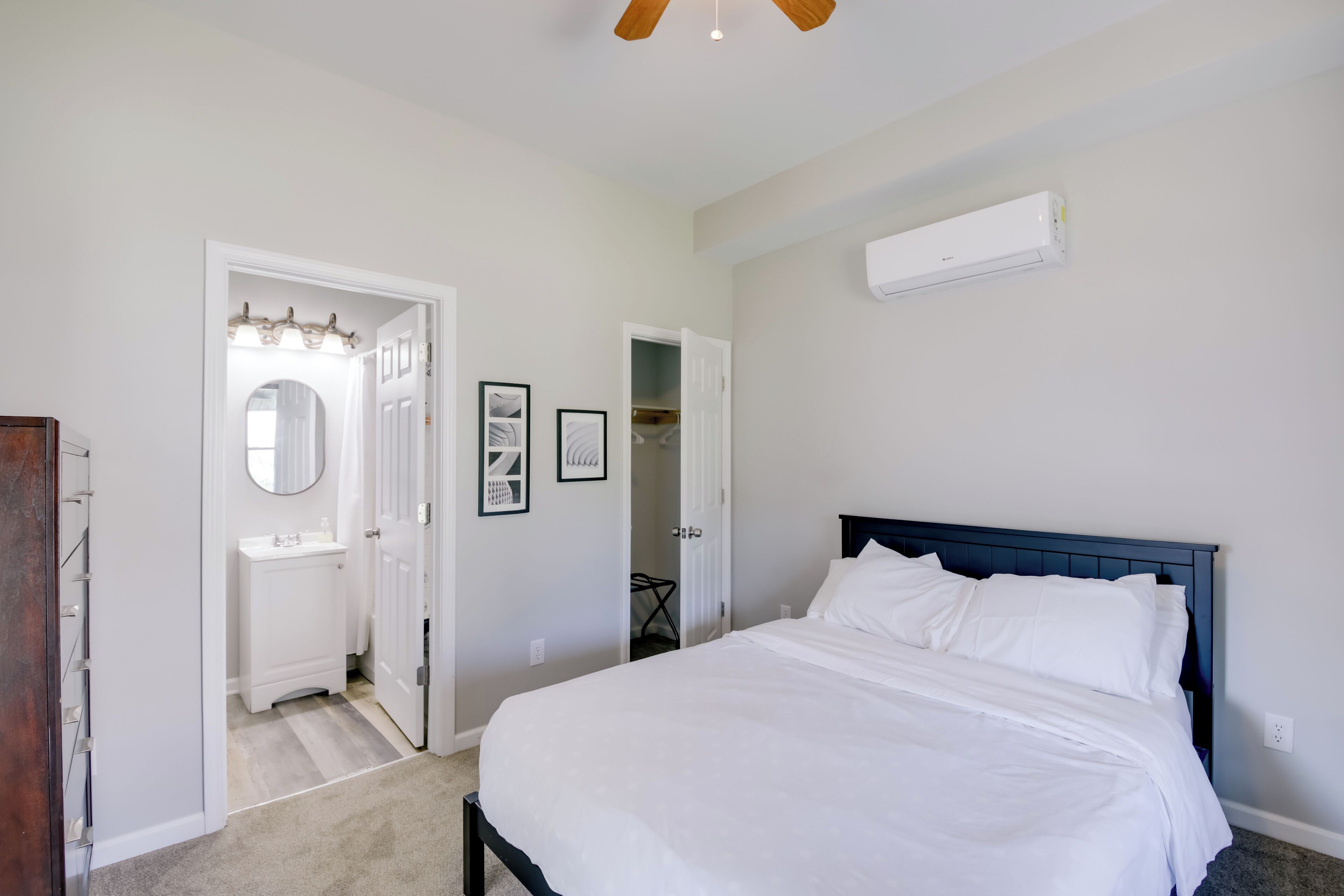 Um quarto com cama, parede branca, ventilador de teto e ar condicionado branco.