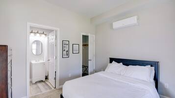 Um quarto com cama, parede branca, ventilador de teto e ar condicionado branco.