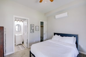 Um quarto com cama, parede branca, ventilador de teto e ar condicionado branco.