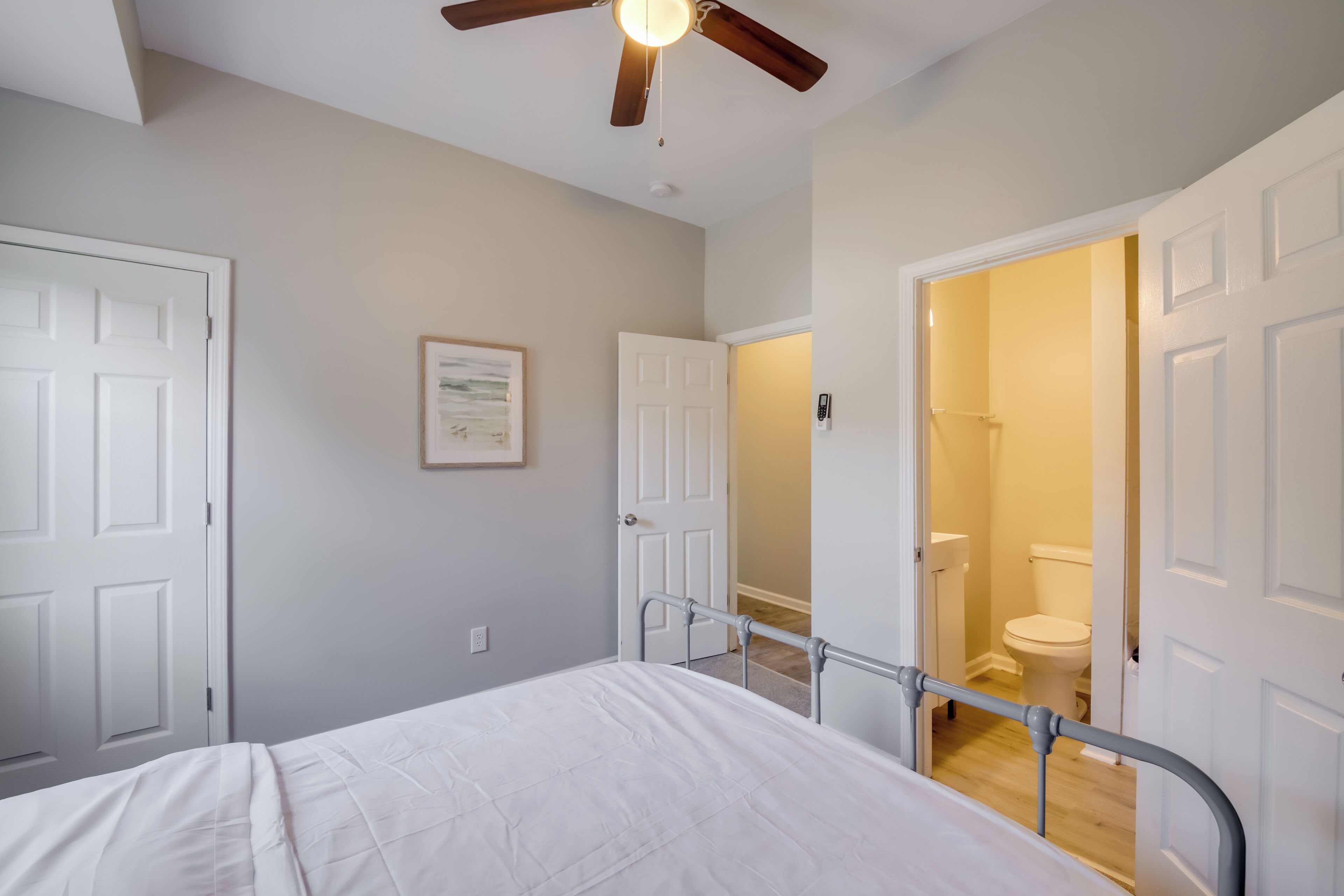 A bedroom with a bed, a ceiling fan, and a door leading to a bathroom.