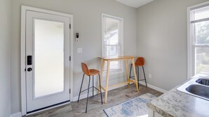 A kitchen with a wooden table and two bar stools, a door with a peephole, and a window with blinds. - Indianapolis Home w/ Porch - Close to Mile Square! (Indianapolis)