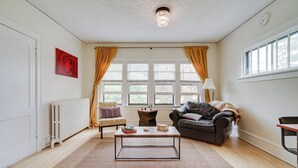 Un salón con una mesa de centro, un sofá, una silla, un radiador y una ventana con cortinas.