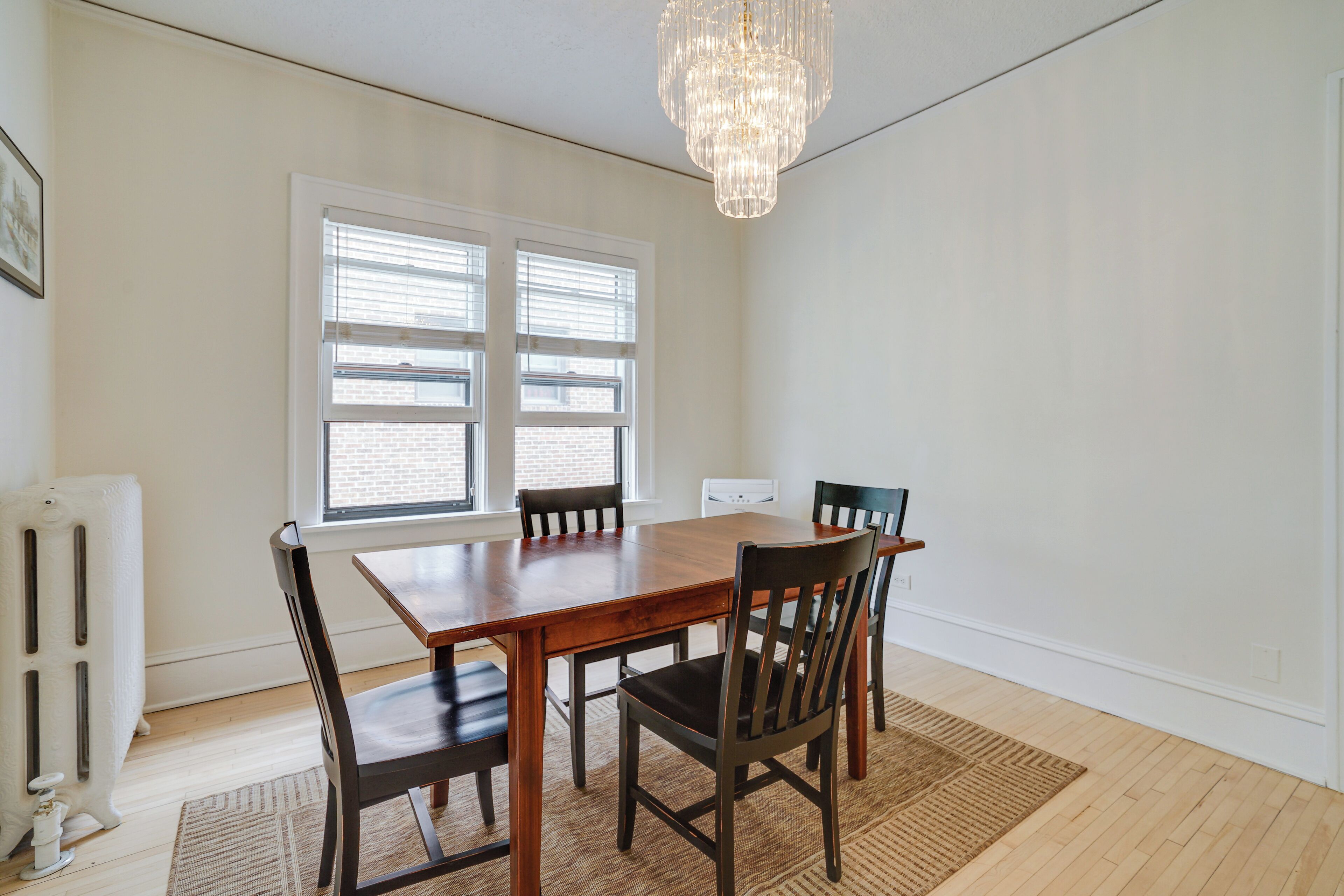 A dining room with a wooden table, four chairs, a chandelier, and a radiator.