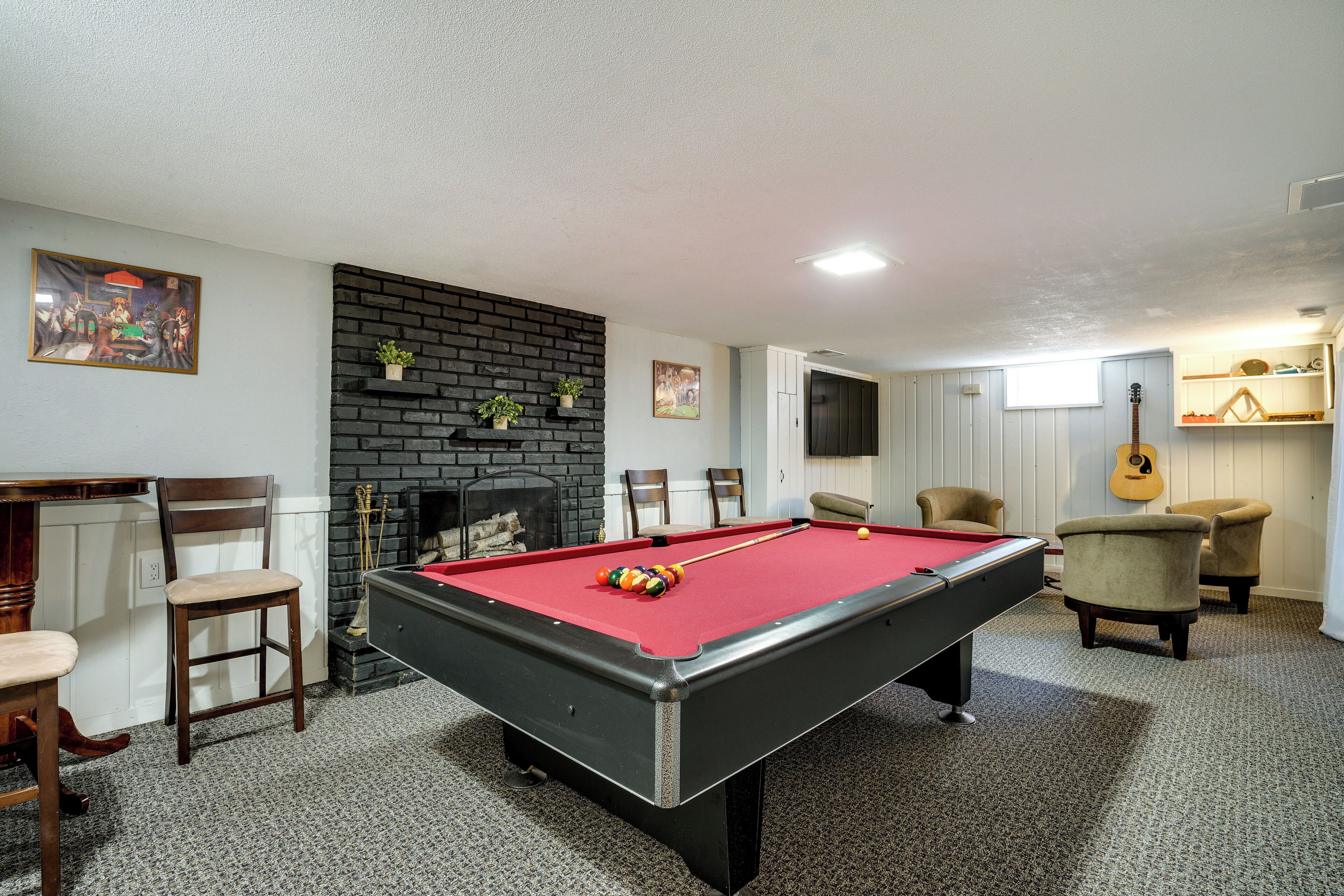 A pool table in a room with a fireplace, chairs, and a guitar wall decoration.