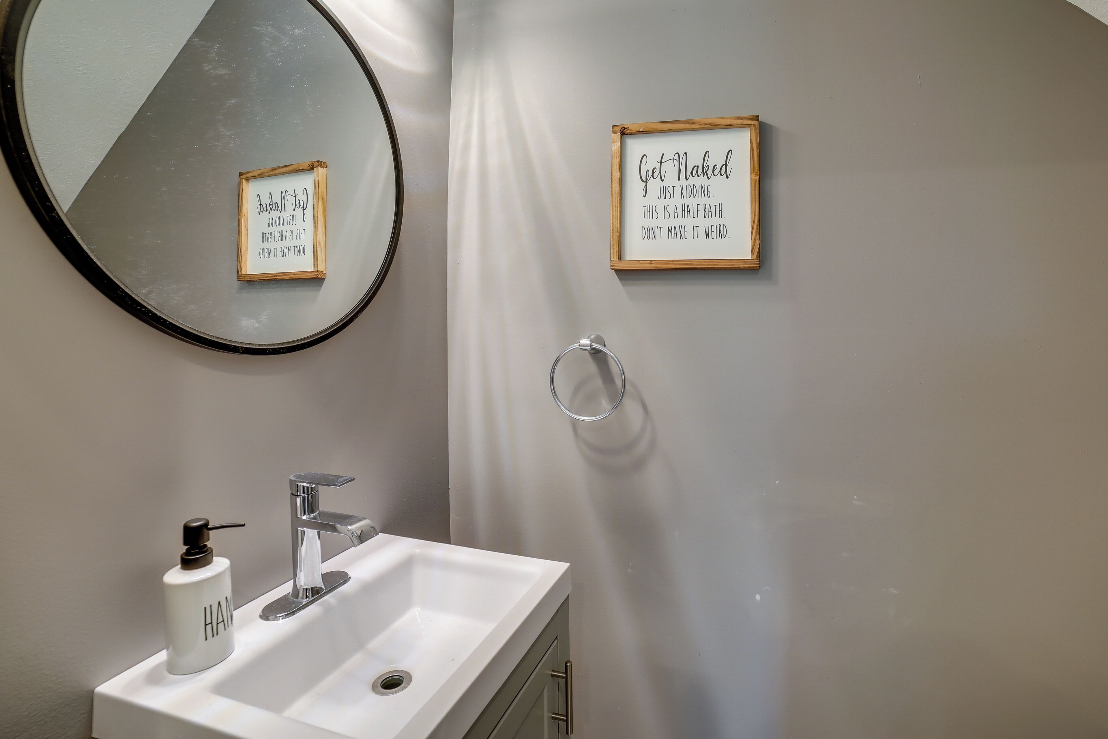 A bathroom with a white sink, a mirror, and two framed signs on the wall.