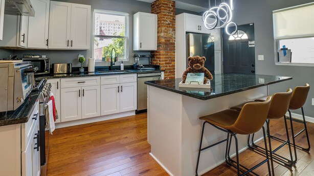 A modern kitchen with white cabinets, a brick accent wall, a stainless steel refrigerator, and a bar area with stools. - Family-friendly Shadyside Gem Near Dtwn Pittsburgh (Pittsburgh)