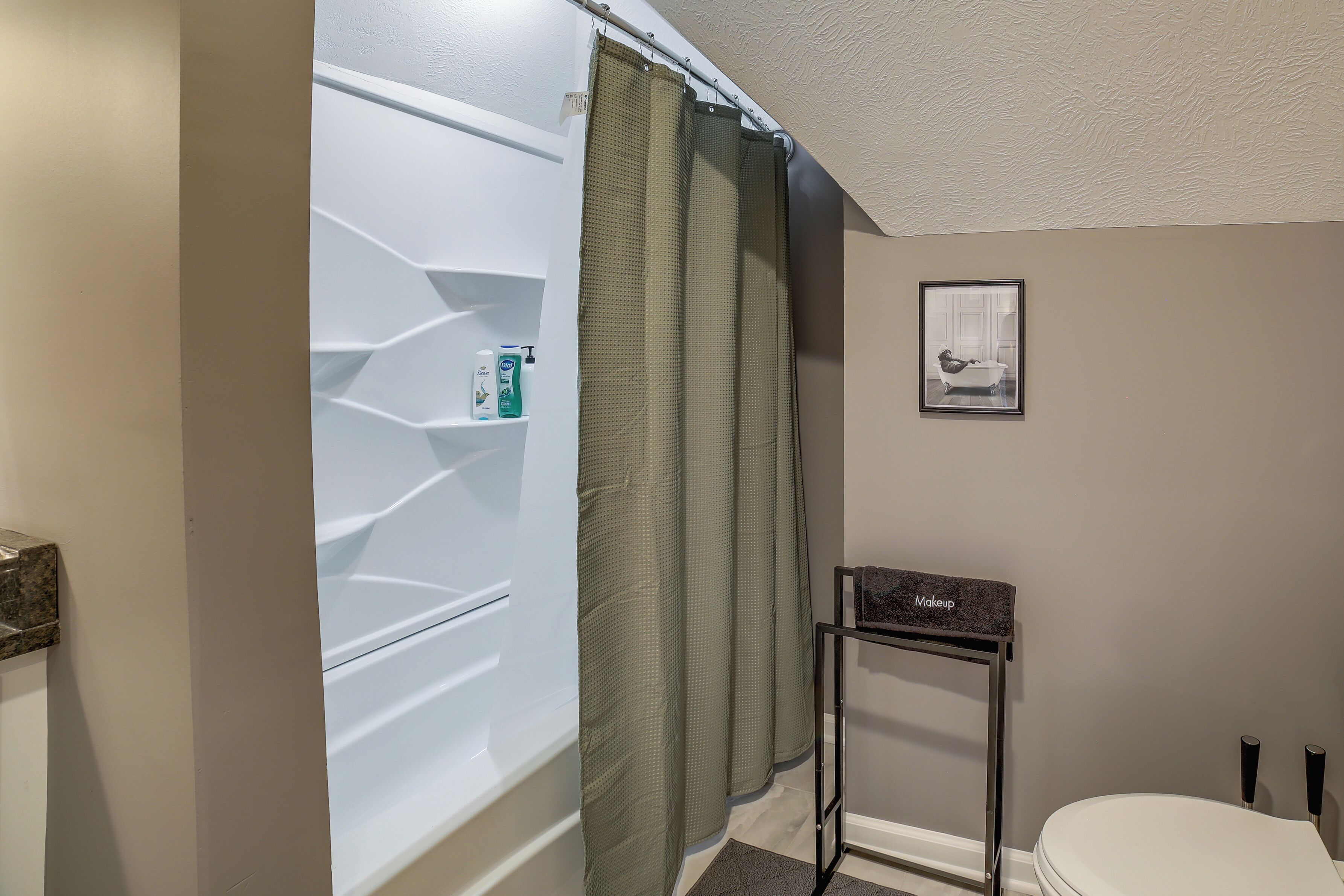 A bathroom with a shower curtain, a framed picture on the wall, and a small table with a towel.