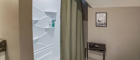 A bathroom with a shower curtain, a framed picture on the wall, and a small table with a towel.