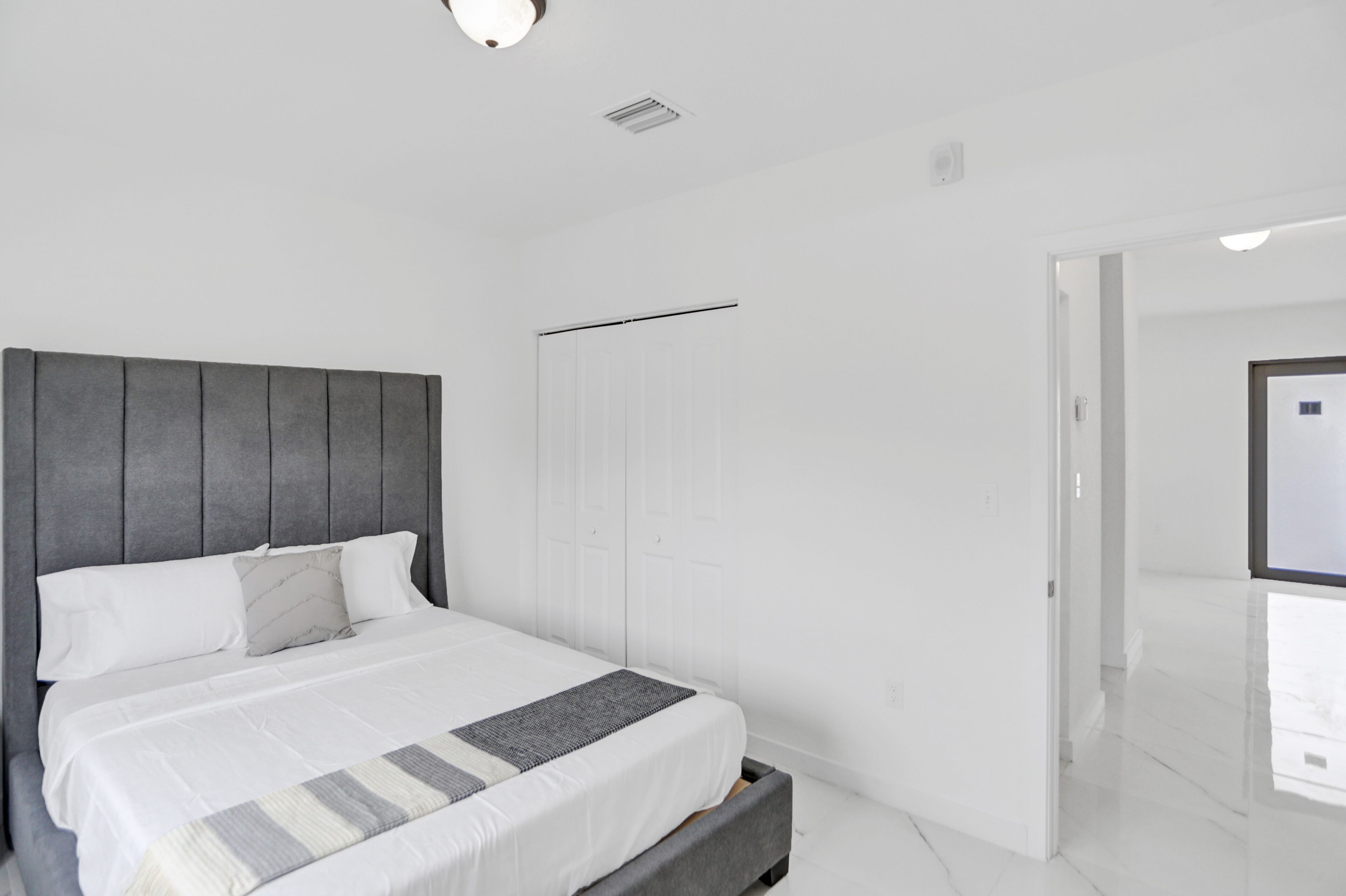 Quarto moderno com cama grande, paredes brancas e cabeceira cinza.