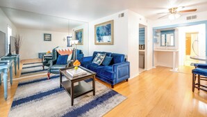 A modern living room with a blue sofa, a coffee table, and a dining area with a blue bench. - Dallas Vacation Rental Condo w/ Community Pool! (Dallas)