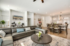 A modern living room with a sectional sofa, a round coffee table, and a dining area with a wooden table and chairs. - Luxury Living: High-rise Balcony 2 Mi to Dtwn ATL (Atlanta)