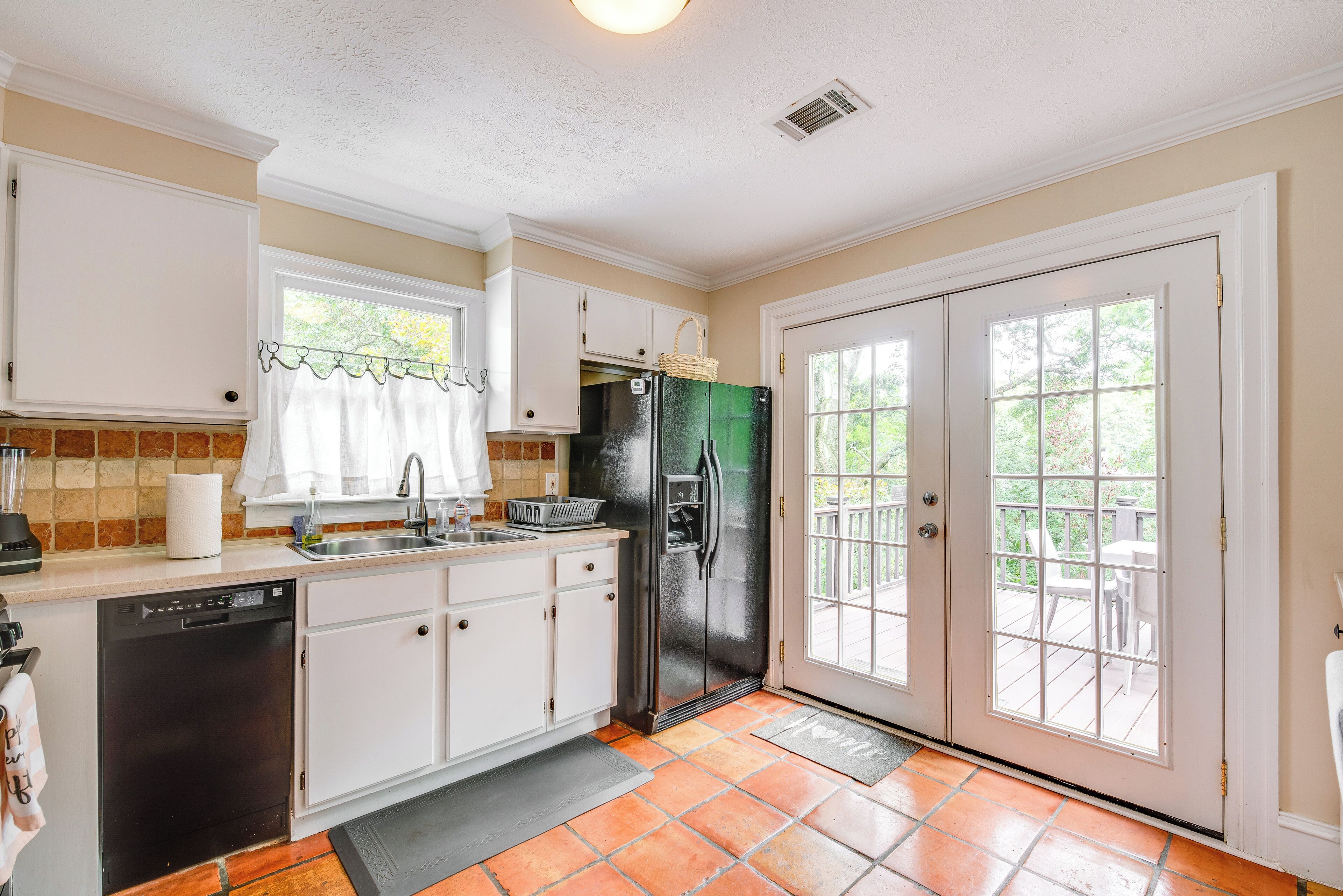 A kitchen with white cabinets, a black dishwasher, a stainless steel refrigerator, and a window with a view of the outdoors.