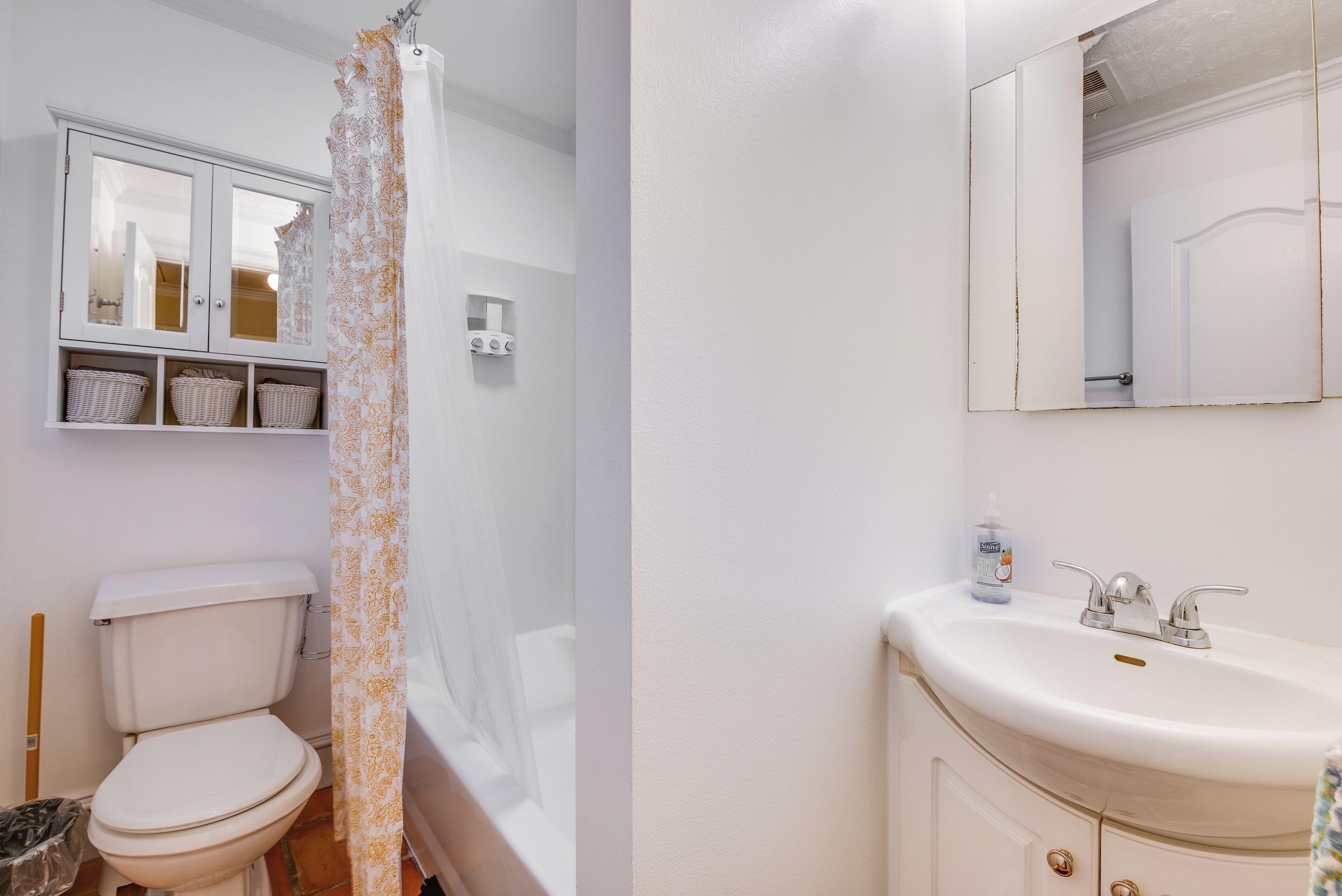 Une salle de bain comprenant des toilettes, un lavabo blanc, un miroir et un meuble avec des paniers.