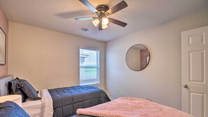 A bedroom with two beds, a ceiling fan, a window with blinds, a round mirror, and a door. - Houston Home w/ Private Yard - 16 Mi to Dtwn (Houston)