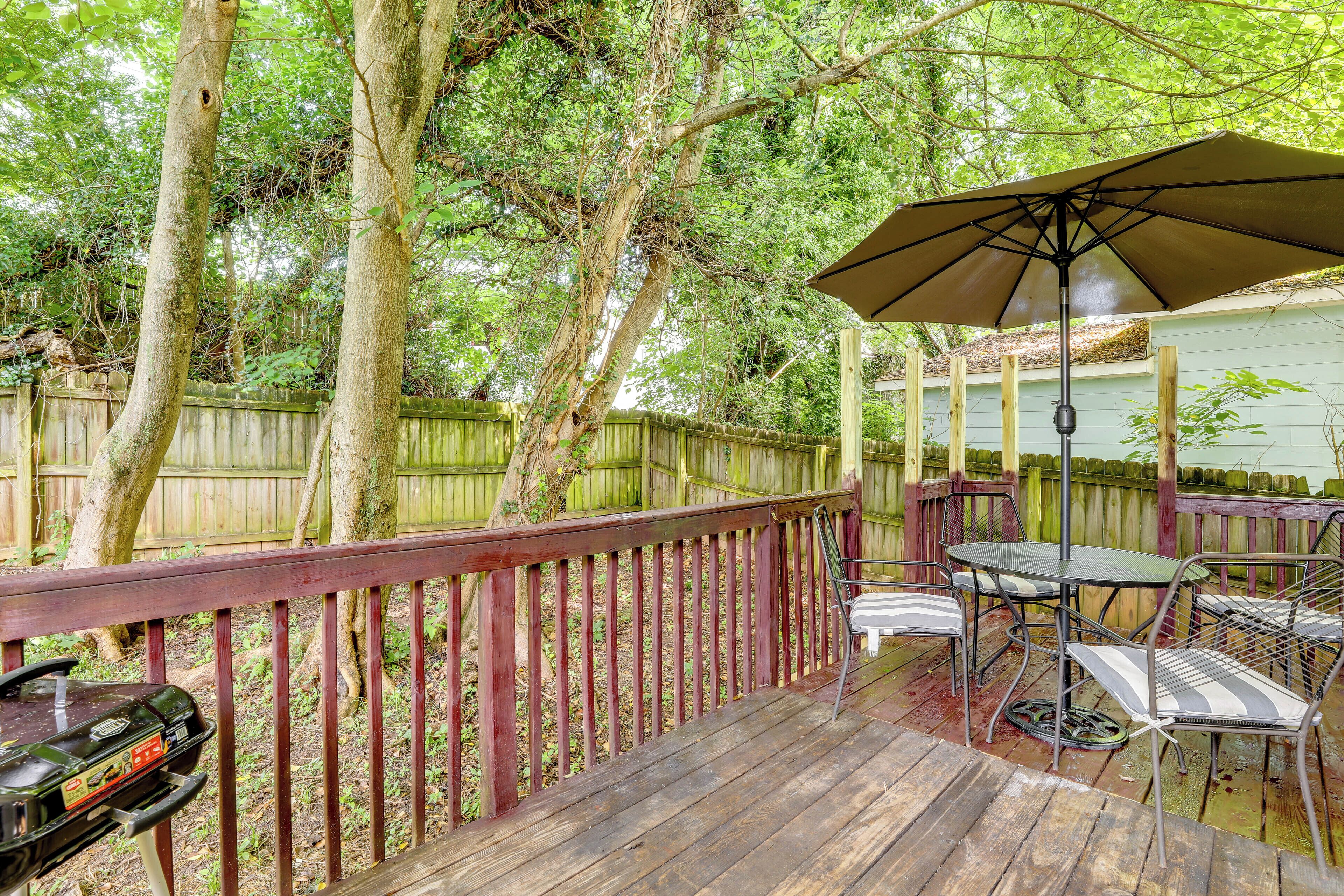 A wooden deck with a barbecue grill, a table with chairs, and an umbrella.