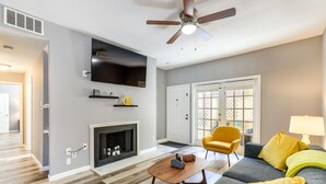 A living room with a fireplace, a ceiling fan, a flat-screen TV, and a yellow armchair. - Houston Rental in Gated Community w/ Pool Access! (Houston)