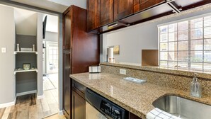 A kitchen with granite countertops, a stainless steel sink, wooden cabinets, and a dishwasher. - Houston Rental in Gated Community w/ Pool Access! (Houston)