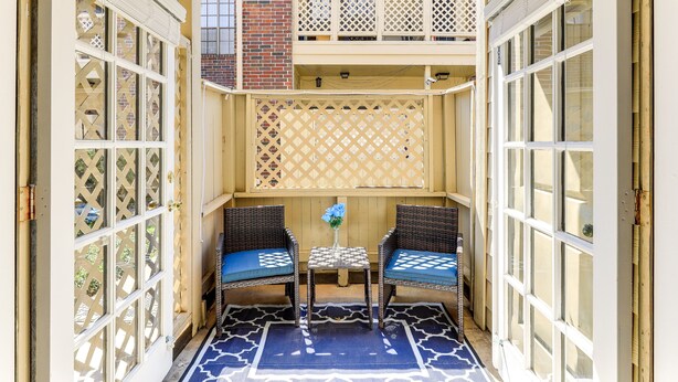 A small outdoor seating area with two wicker chairs and a table, enclosed by a lattice fence and a wooden door. - Houston Rental in Gated Community w/ Pool Access! (Houston)