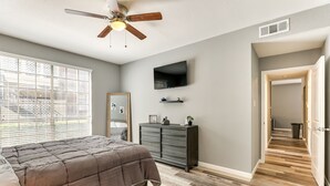 A bedroom with a bed, a ceiling fan, a dresser, a TV, and a hallway with wooden flooring. - Houston Rental in Gated Community w/ Pool Access! (Houston)