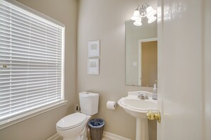 Bathroom features a toilet, sink, and mirror, with a window and wall-mounted light.