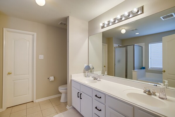 Bathroom features a large mirror above a single sink with a faucet and soap dispenser, a toilet, and a door to another room.