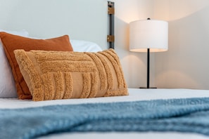 A neatly made bed with a blue blanket, a fluffy beige pillow, and a white pillow.