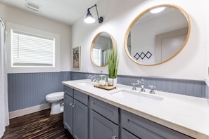 A bathroom with a white sink, two round mirrors, a toilet, and a shower curtain.
