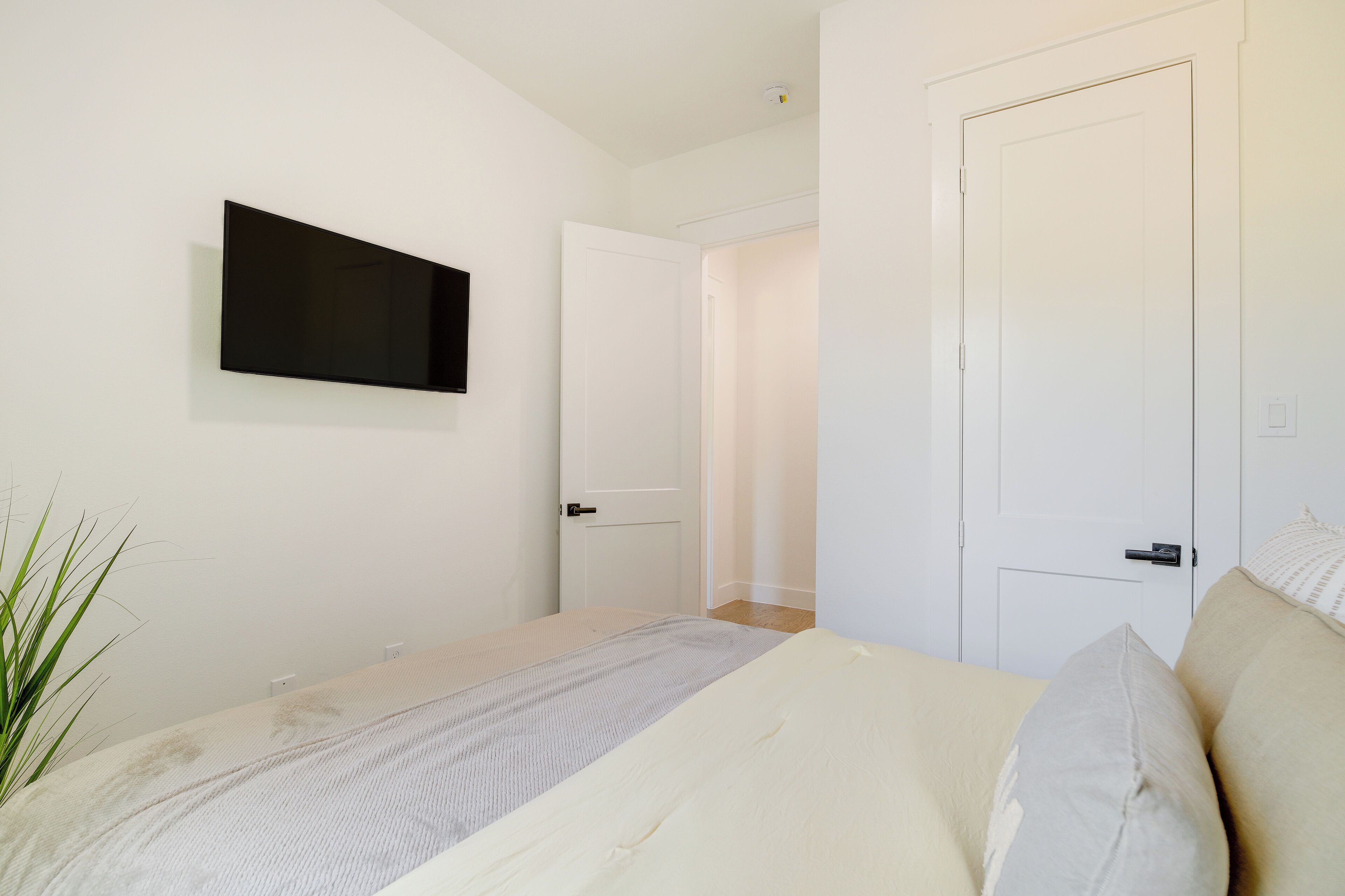 Un dormitorio con cama, televisor montado en la pared y puerta que da a otra habitación.