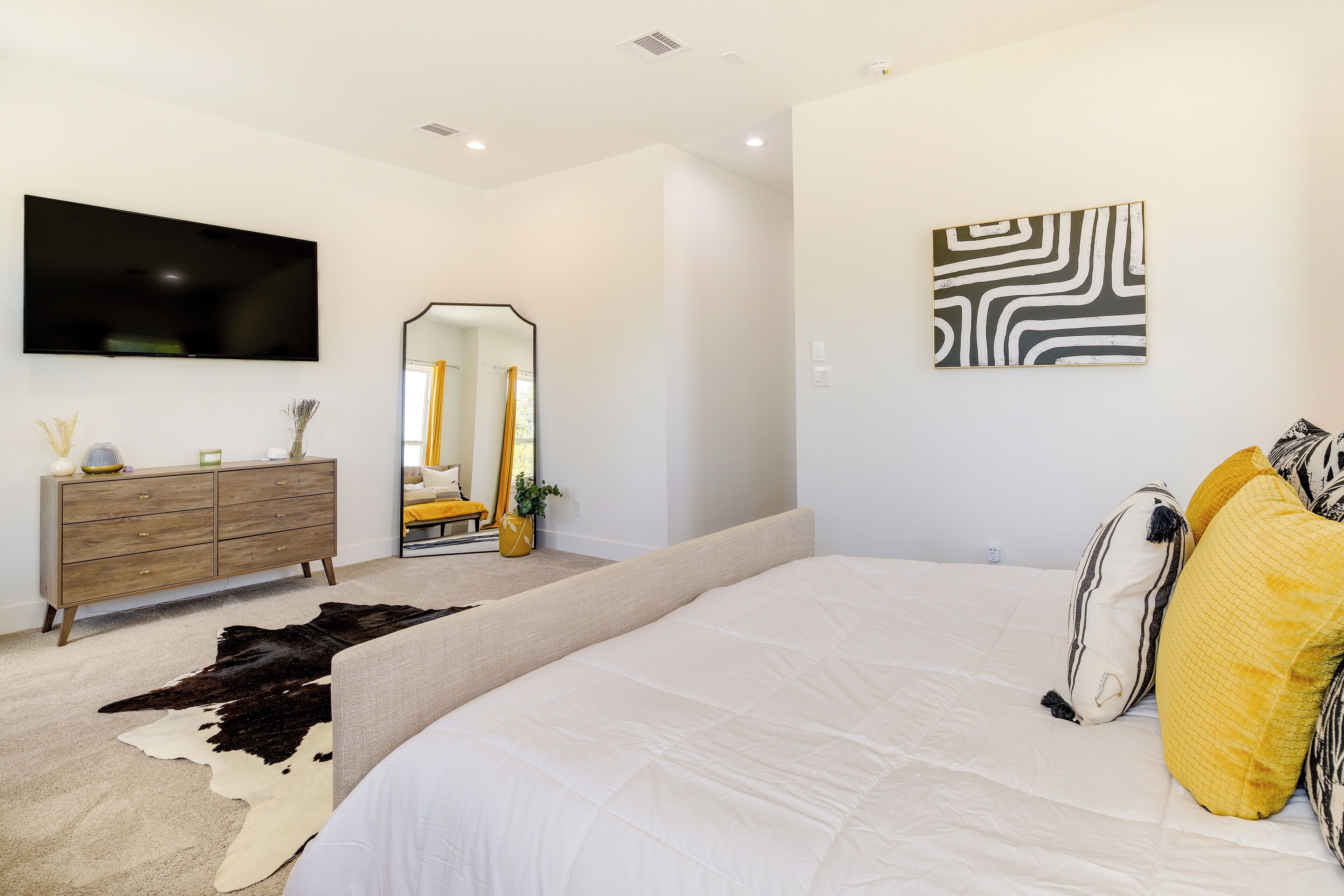A modern bedroom with a large bed, a flat-screen TV, a dresser, and a mirror.