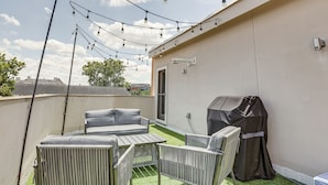 A rooftop patio with a grill, outdoor furniture, and string lights. - Houston Retreat With Fireplace & Balcony! (Houston)