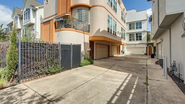A multi-story residential building with a garage, a fenced yard, and a clear sky. - Houston Retreat With Fireplace & Balcony! (Houston)