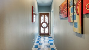 A hallway with a checkered floor, a wooden door with a glass window, and abstract paintings on the wall. - Houston Retreat With Fireplace & Balcony! (Houston)