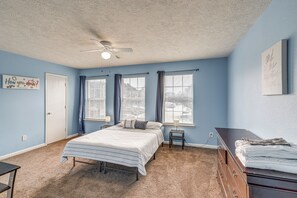 Ein Schlafzimmer mit Bett, Schminktisch, Deckenventilator und zwei mit Vorhängen versehenen Fenstern.