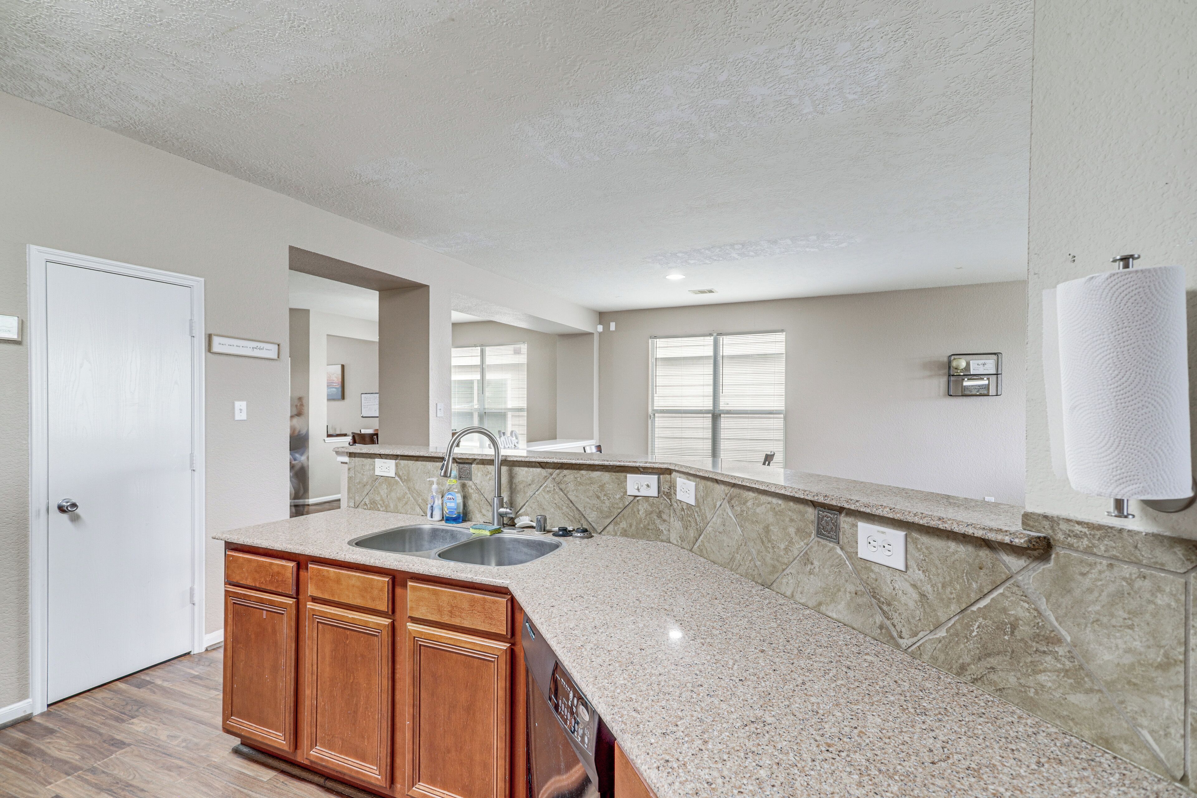 A kitchen with granite countertops, wooden cabinets, a double sink, and a window with blinds.