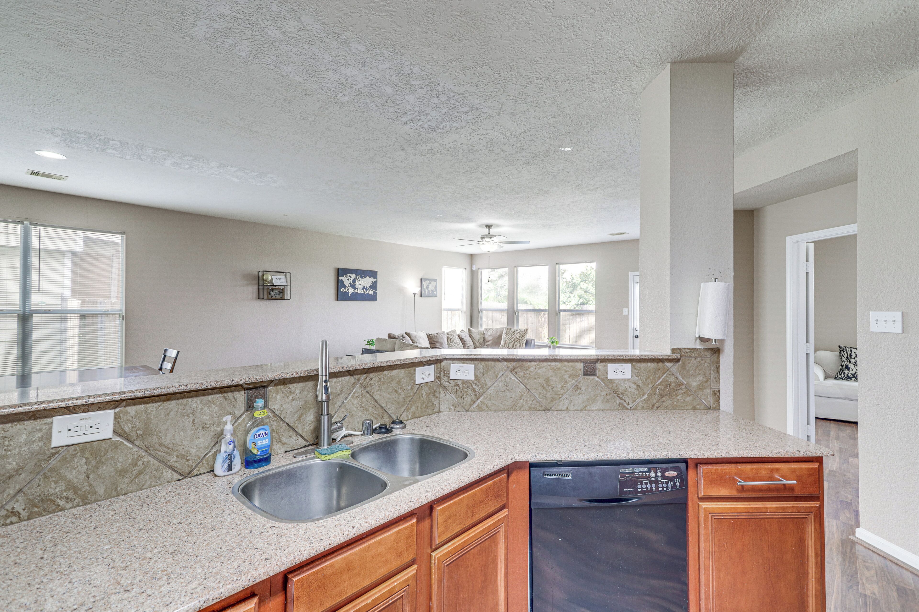 A kitchen with granite countertops, wooden cabinets, a dishwasher, and a double sink.