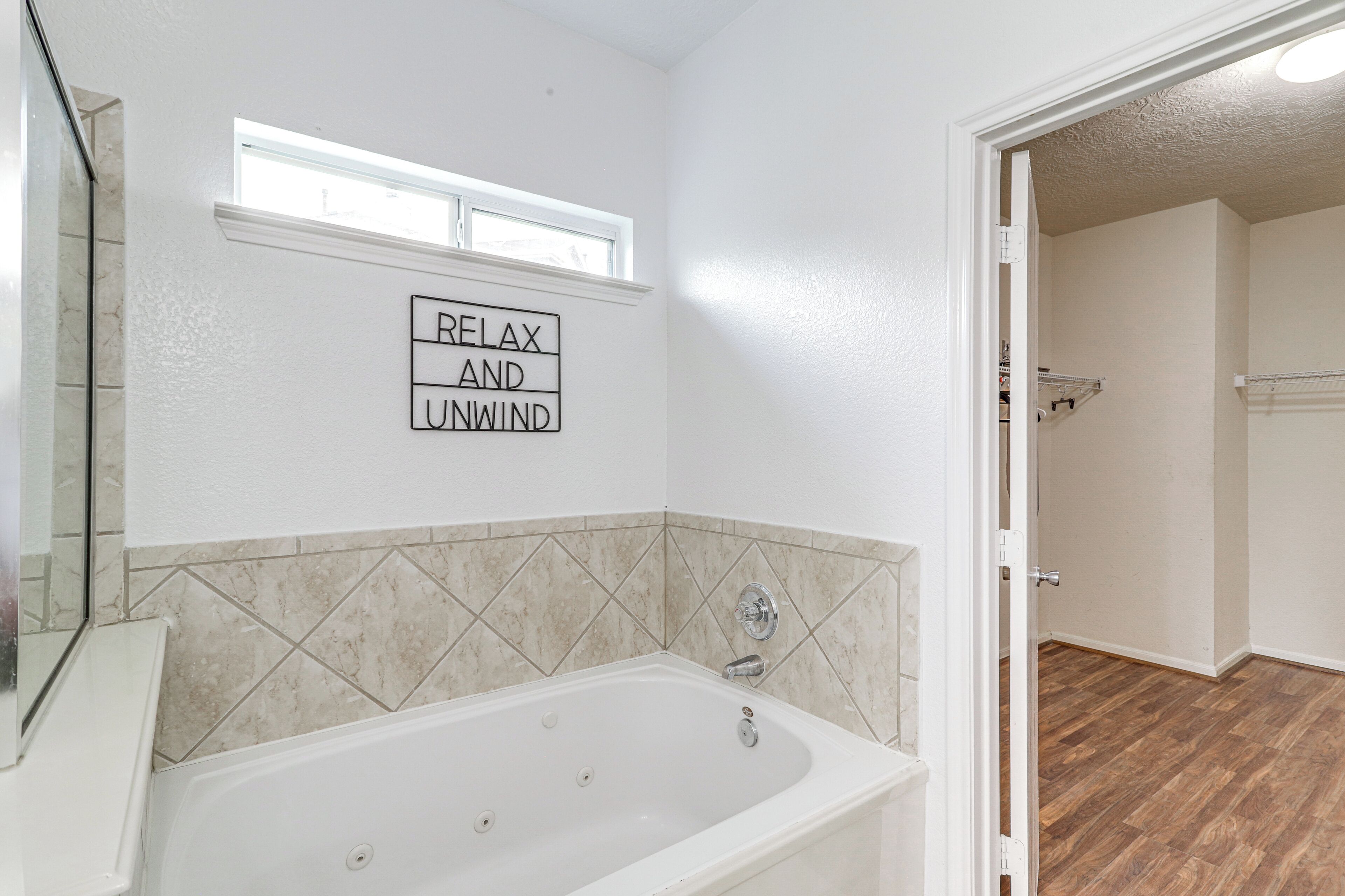 Une salle de bain avec une baignoire, un panneau fixé au mur sur lequel on peut lire « DÉTENDEZ-VOUS ET RELÂCHEZ-VOUS », et une fenêtre au-dessus de la baignoire.