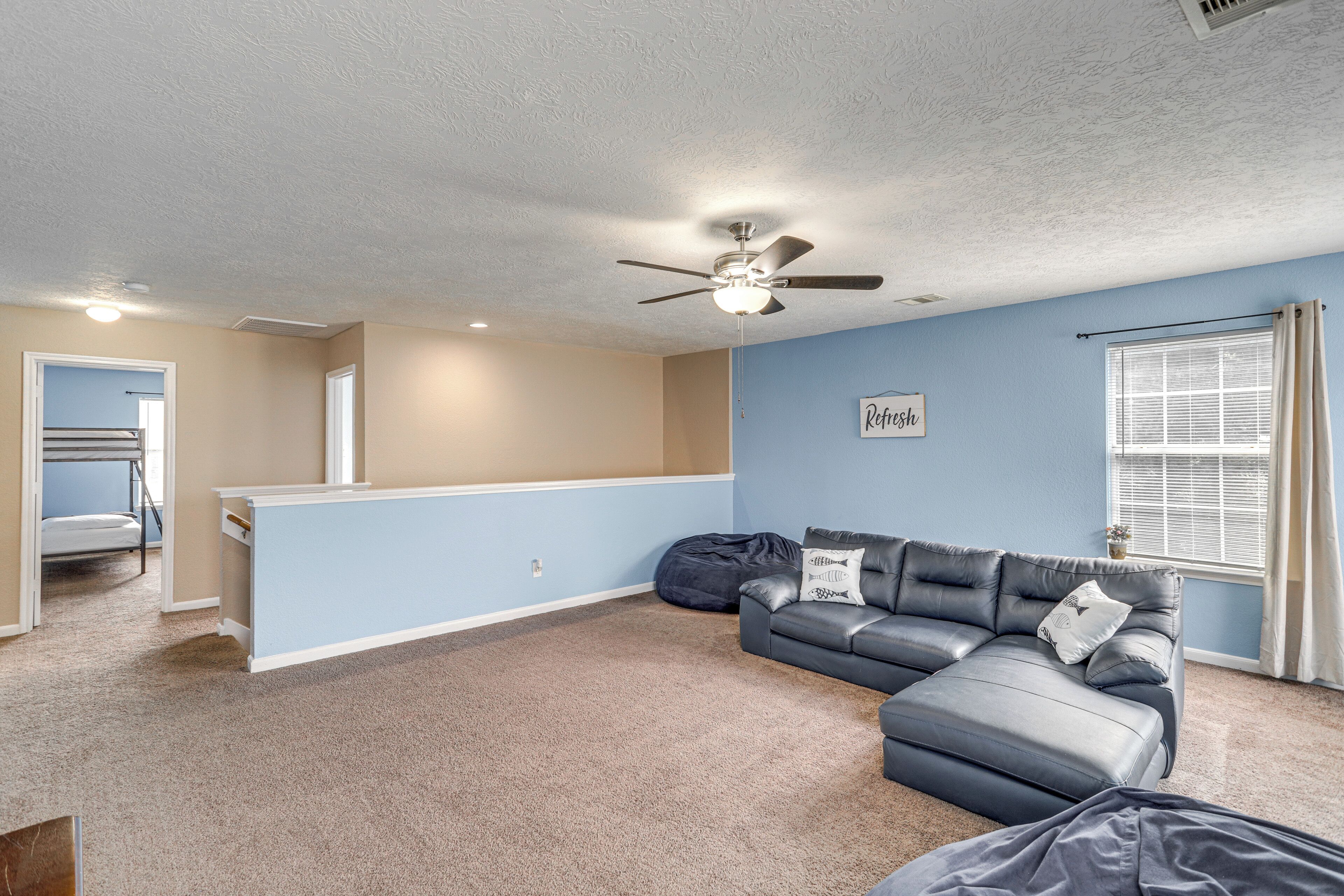 A living room with a sectional sofa, a ceiling fan, and a window with blinds.