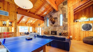 A spacious room with a ping pong table, a stone fireplace, and a stone wall with a mounted animal head.