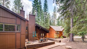 A cabin with a deck, wooden furniture, and a view of surrounding trees.
