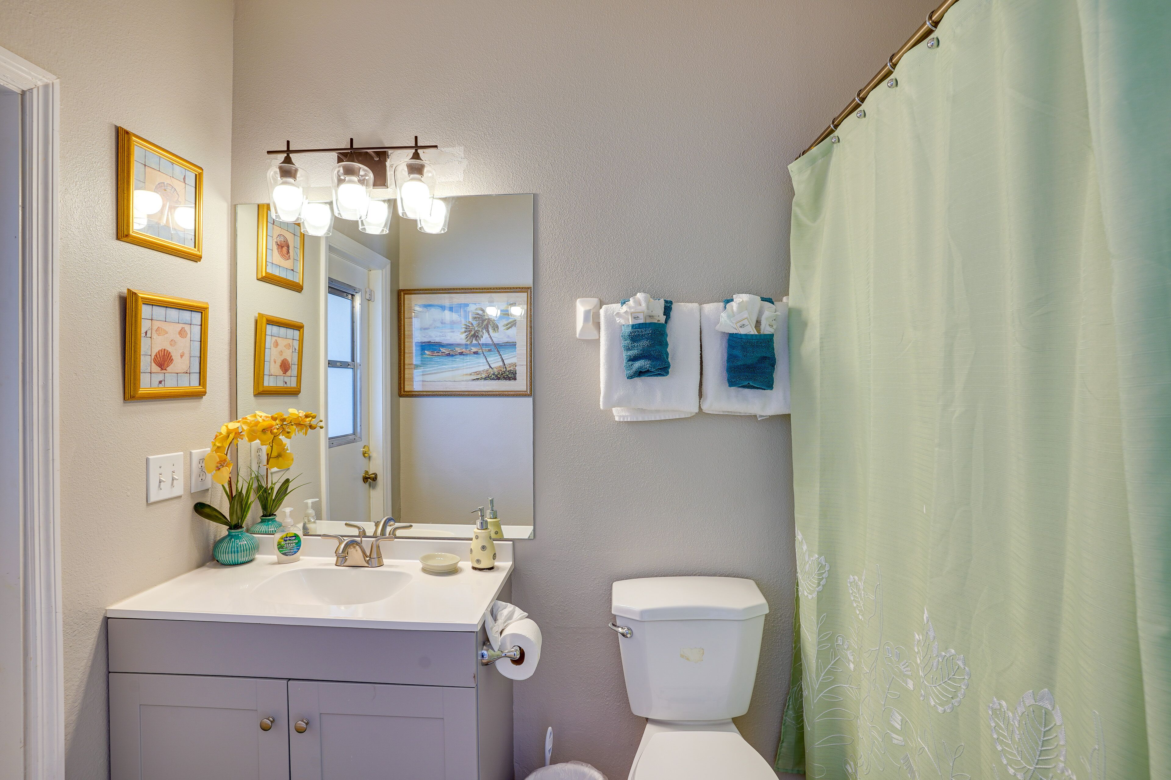 A bathroom with a white sink, mirror, and toilet. There are framed pictures on the wall, a shower curtain, and towels hanging on the wall.