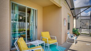 A covered outdoor seating area with two yellow cushioned chairs and a small table, a glass door leading to a pool, and a sign indicating a no-smoking policy. - Florida Retreat w/ Pool, Hot Tub & Near Disney! (Davenport)