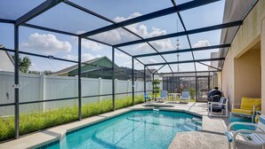 A covered outdoor swimming pool with a glass enclosure, surrounded by a white fence, and equipped with lounge chairs and a table. - Florida Retreat w/ Pool, Hot Tub & Near Disney! (Davenport)