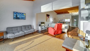 A spacious living area with a grey sofa, a red chair, and a wooden coffee table. There is a painting on the wall and a television on a white cabinet. - Waterfront Haines City Vacation Rental w/ Pool! (Haines City)