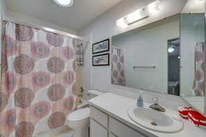 Een badkamer met douchegordijn, toilet, wastafel en spiegel.